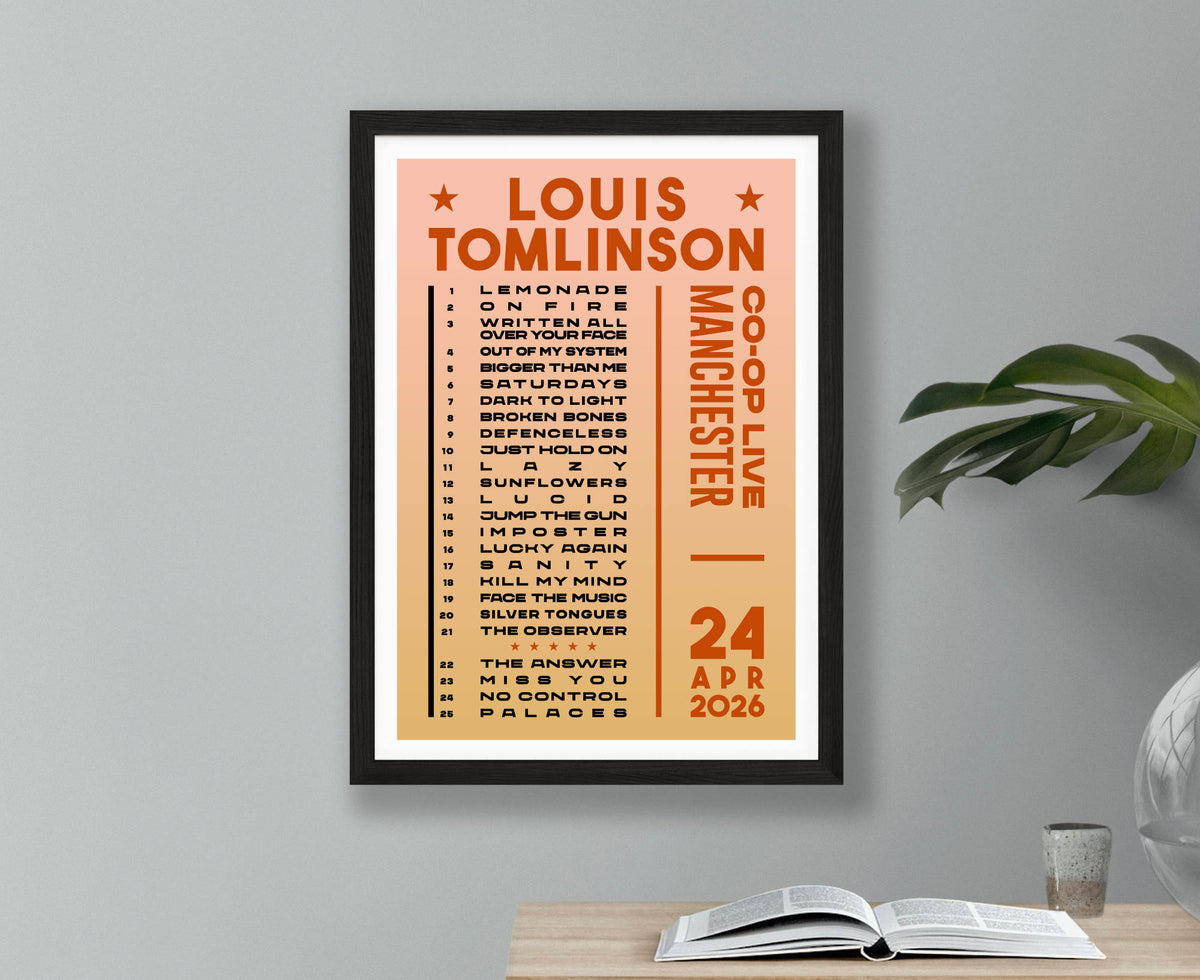 A framed Louis Tomlinson Manchester concert setlist poster for 24 April 2026. Displayed on a light gray wall above a desk with an open book and a plant.